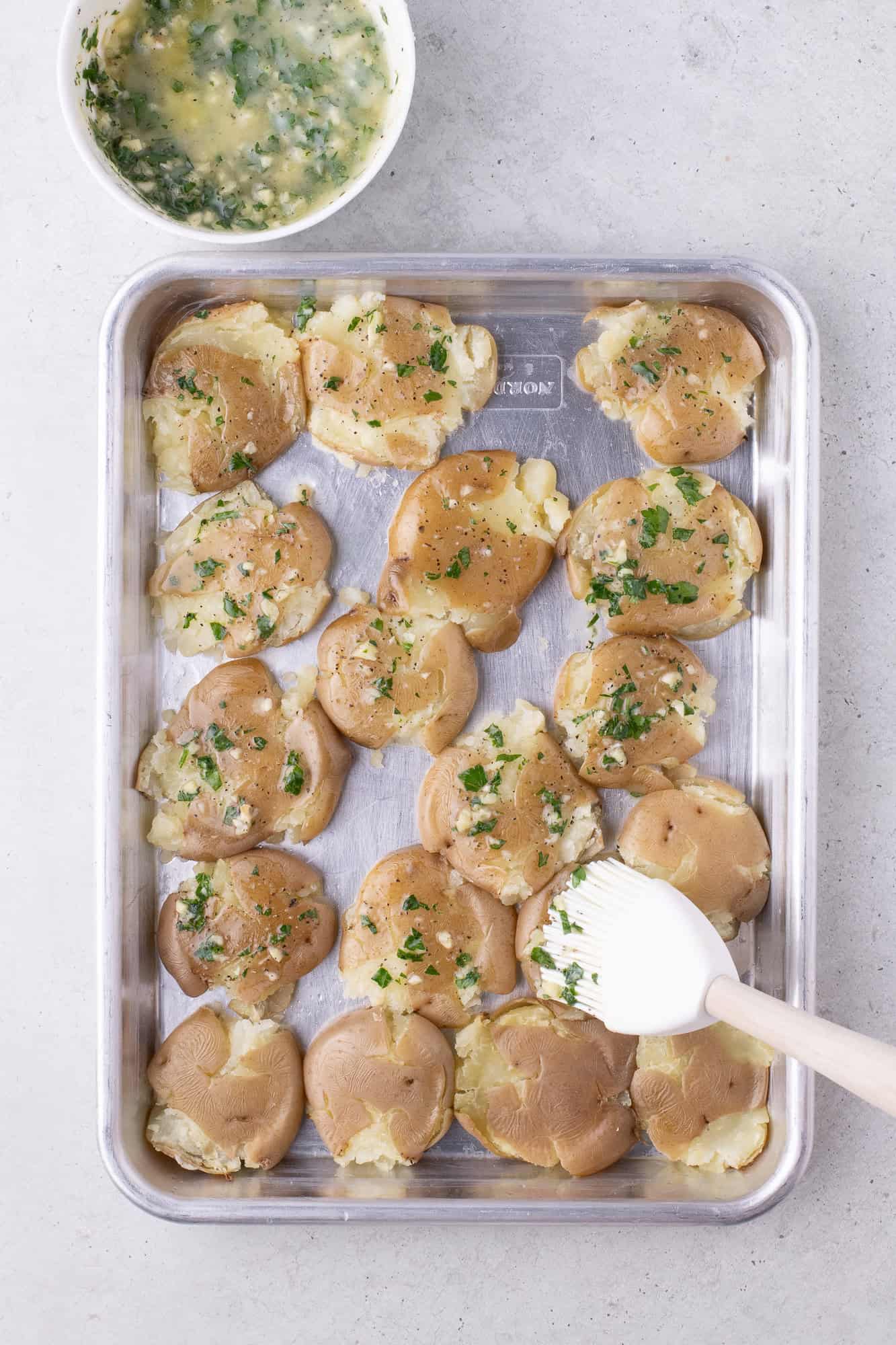 Garlic butter being brushed on smashed potatoes.