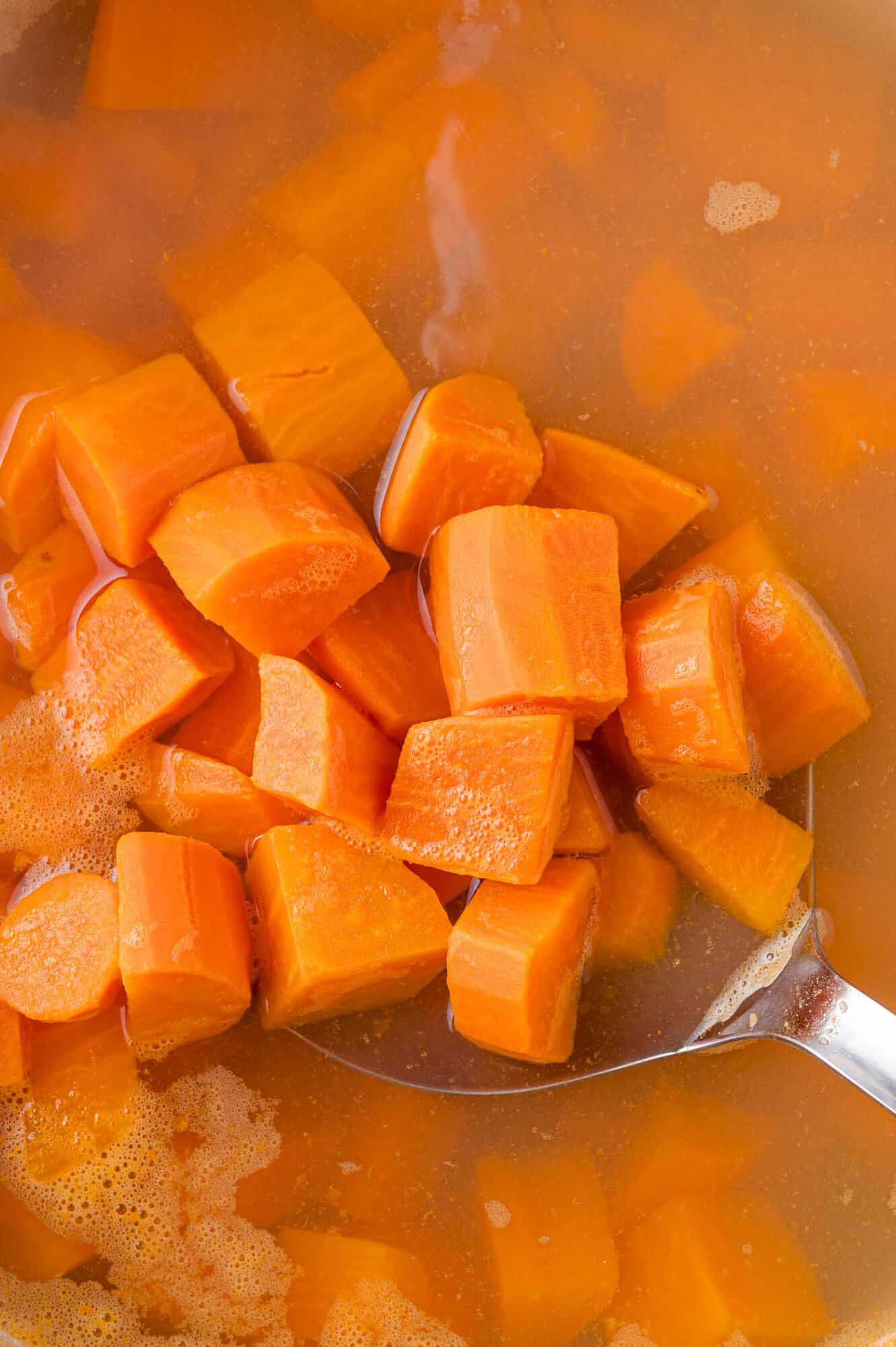 Sweet potato chunks being lifted out of boiling water.