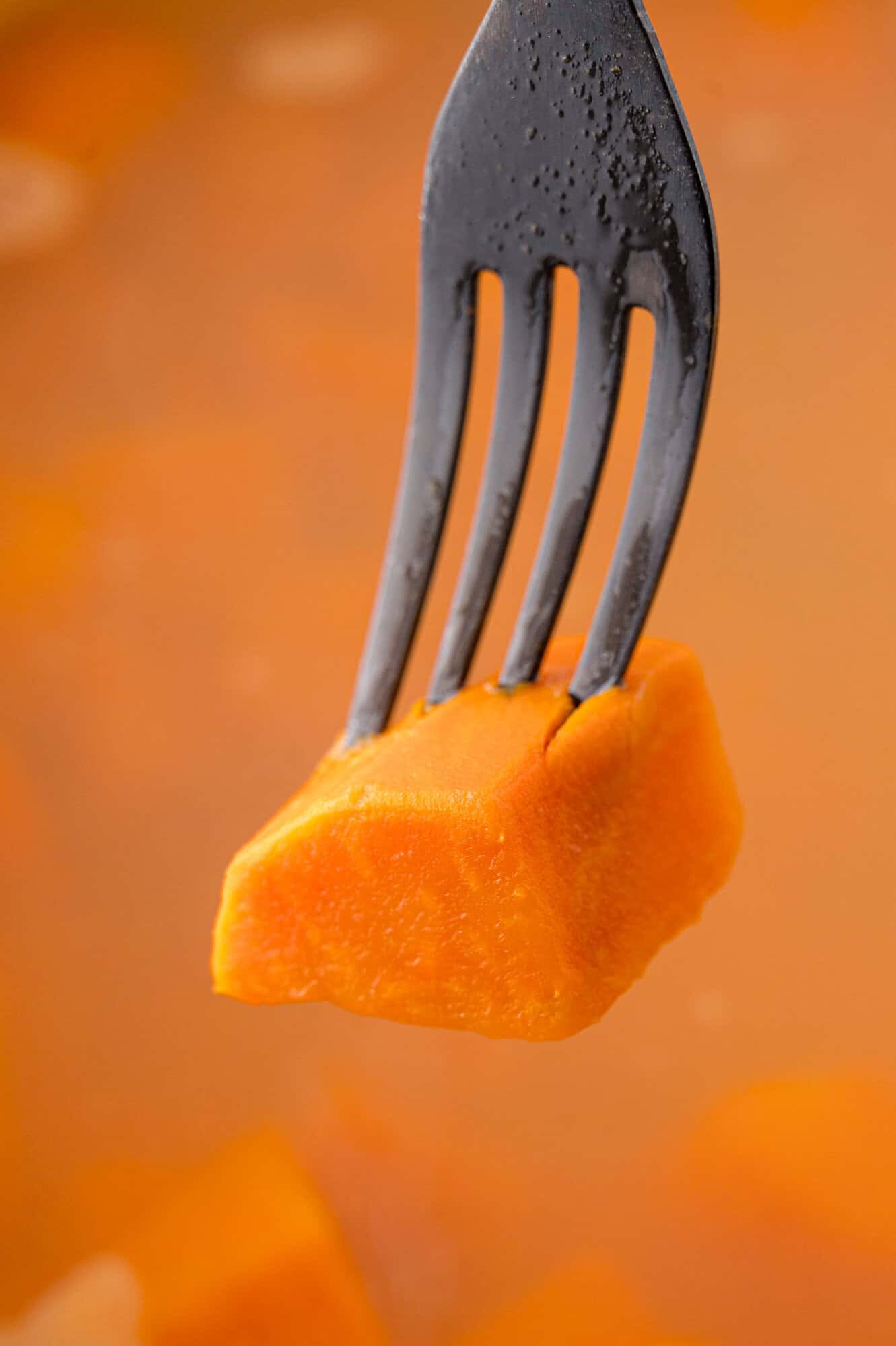 Fork stuck in a sweet potato chunk, showing its tenderness.