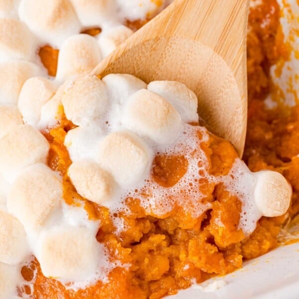 Sweet potato casserole, topped with marshmallows, being scooped with a wooden spoon.