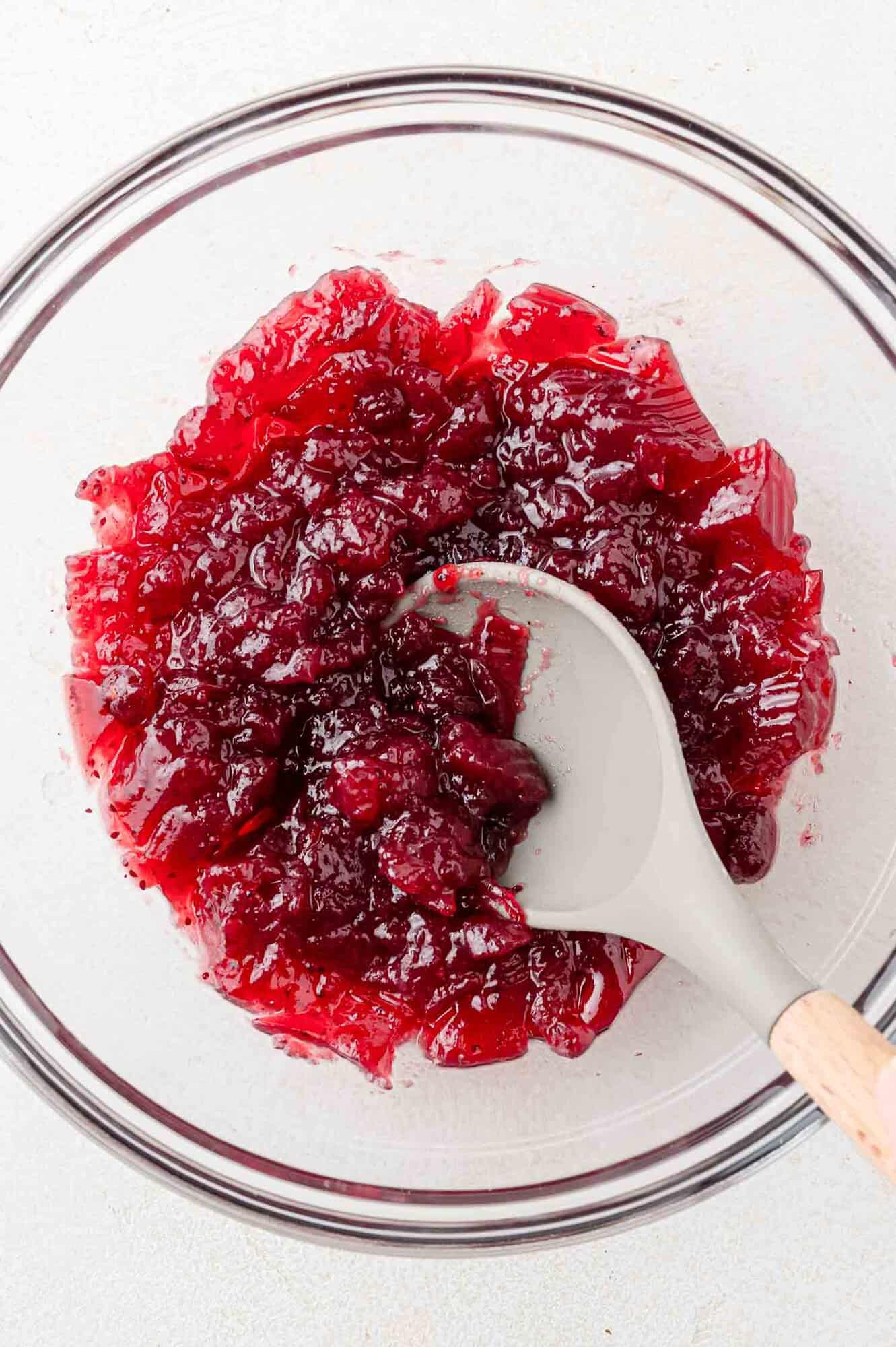 Cranberry sauce being mashed slightly with a spoonn.