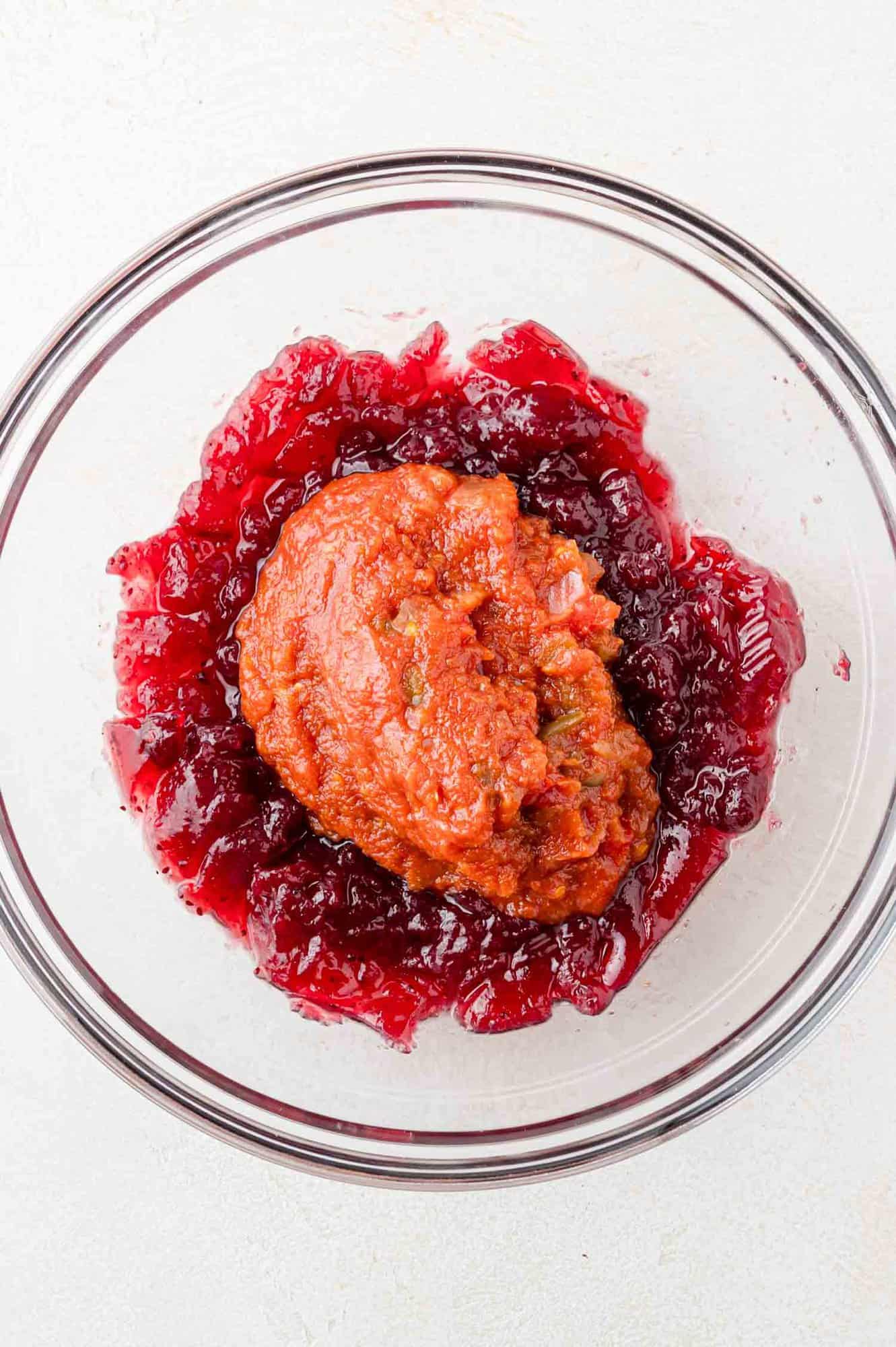 Cranberry sauce and salsa in a clear glass bowl, not yet mixed together.