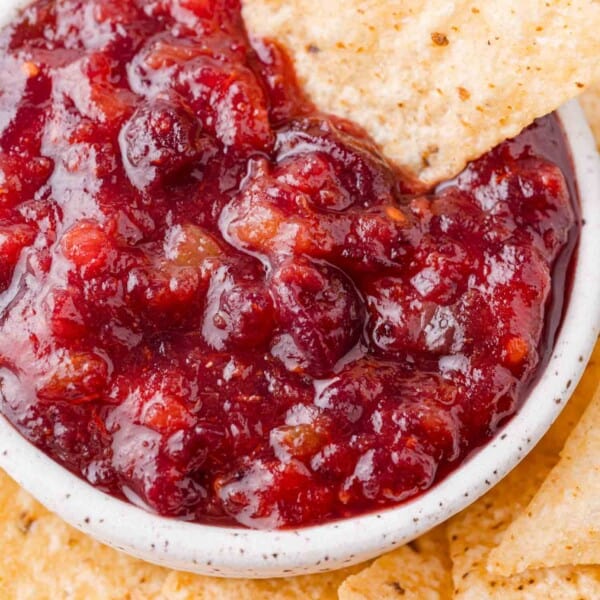 Cranberry salsa in a white bowl, with a chip dipping into it.