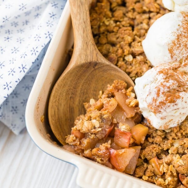 Close up view of apple crisp with ginger, topped with ice cream, being scooped with wooden spoon.