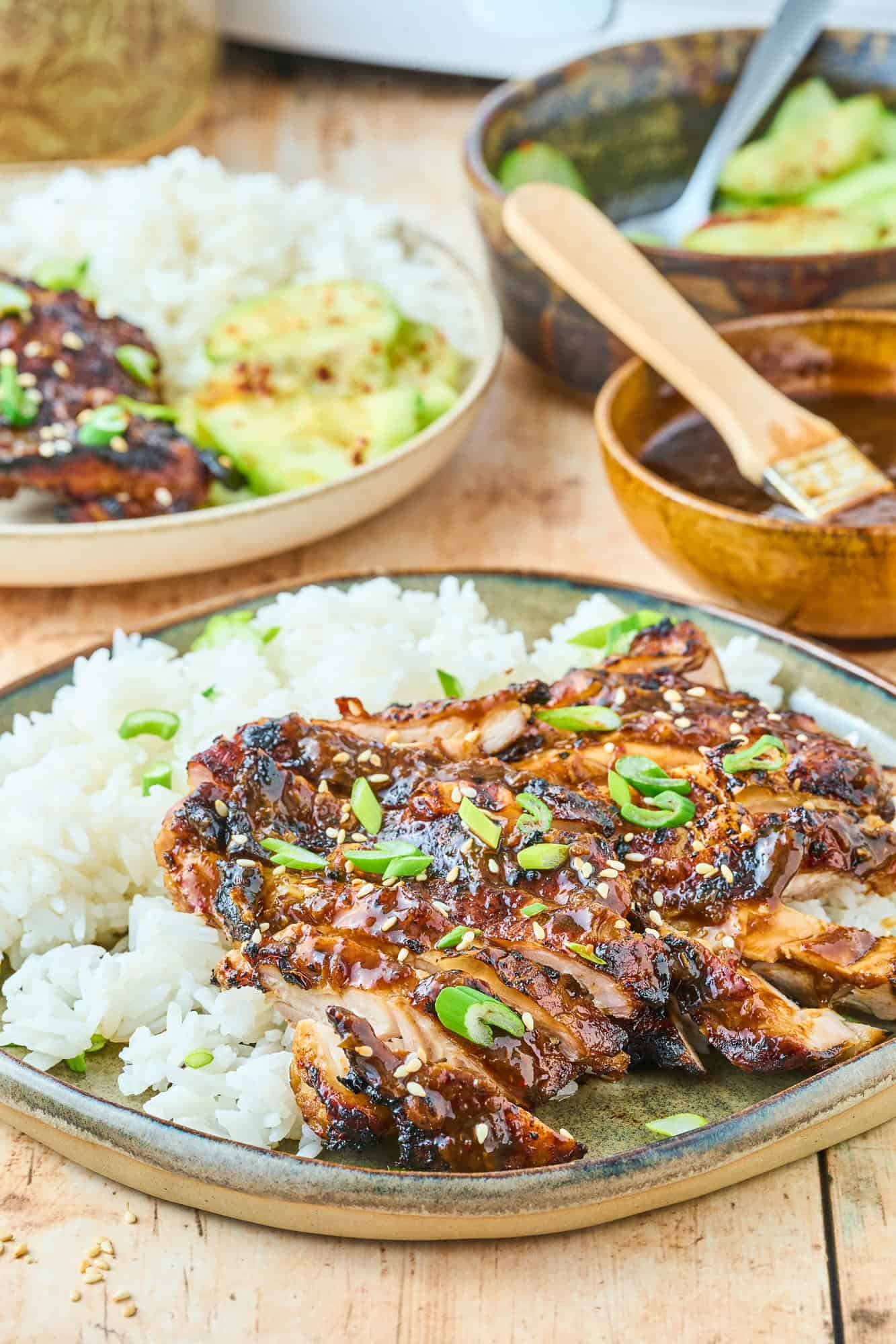 Sliced chicken thigh on rice, another plate of food in the background.