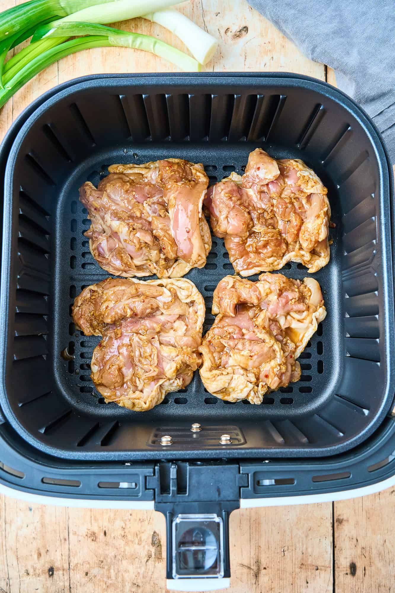 Uncooked chicken thighs in air fryer basket.
