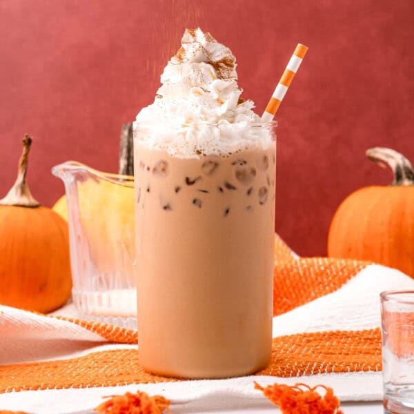 Iced pumpkin spice latte topped with whipped cream, against orange background.