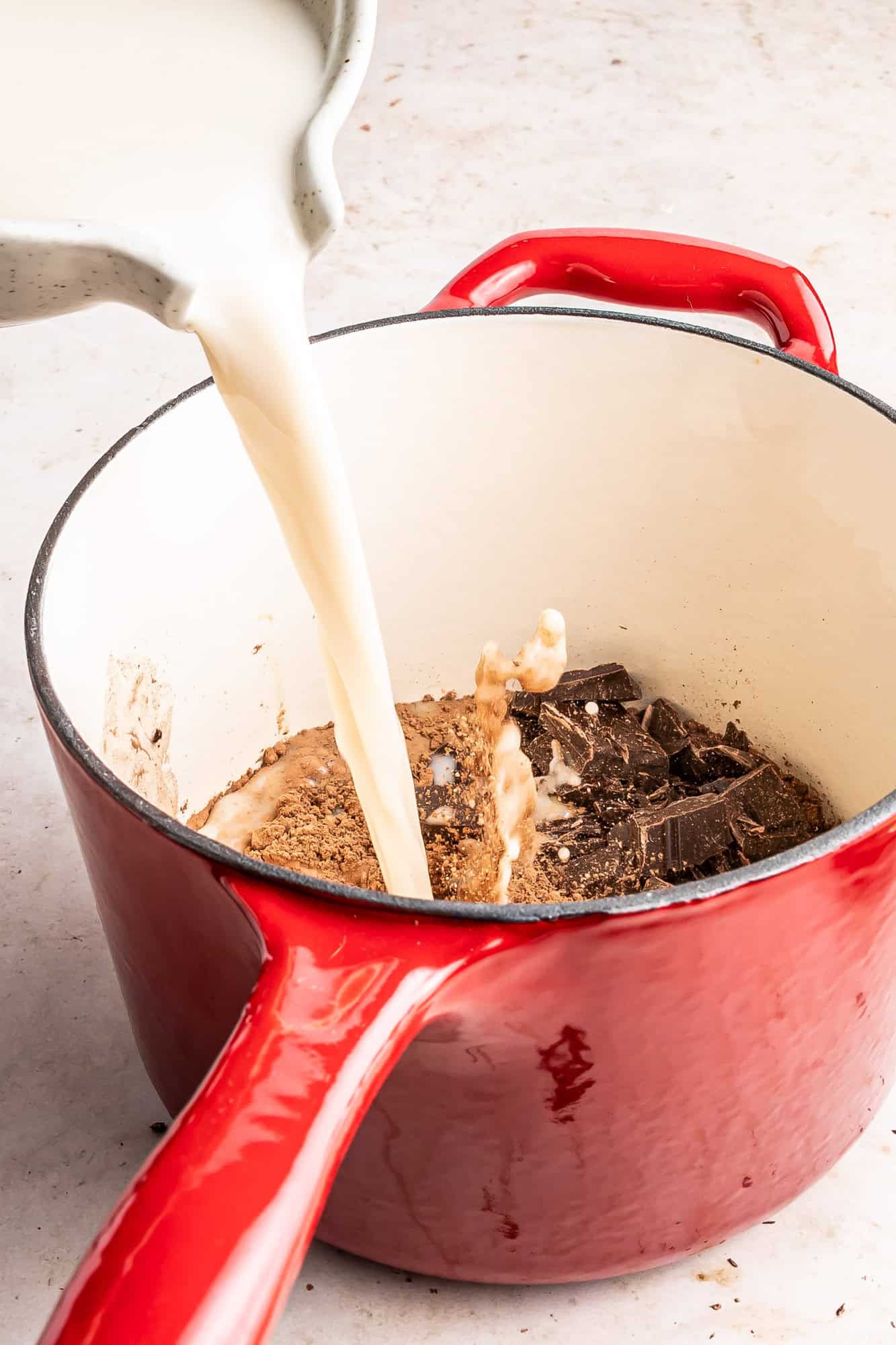 Oat milk being poured into small red saucepan.