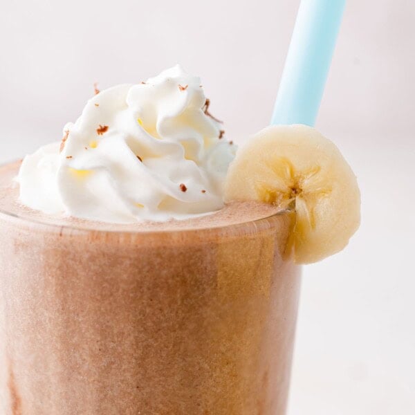 Chocolate milkshake with whipped cream and a banana slice on the rim, featuring a blue straw.