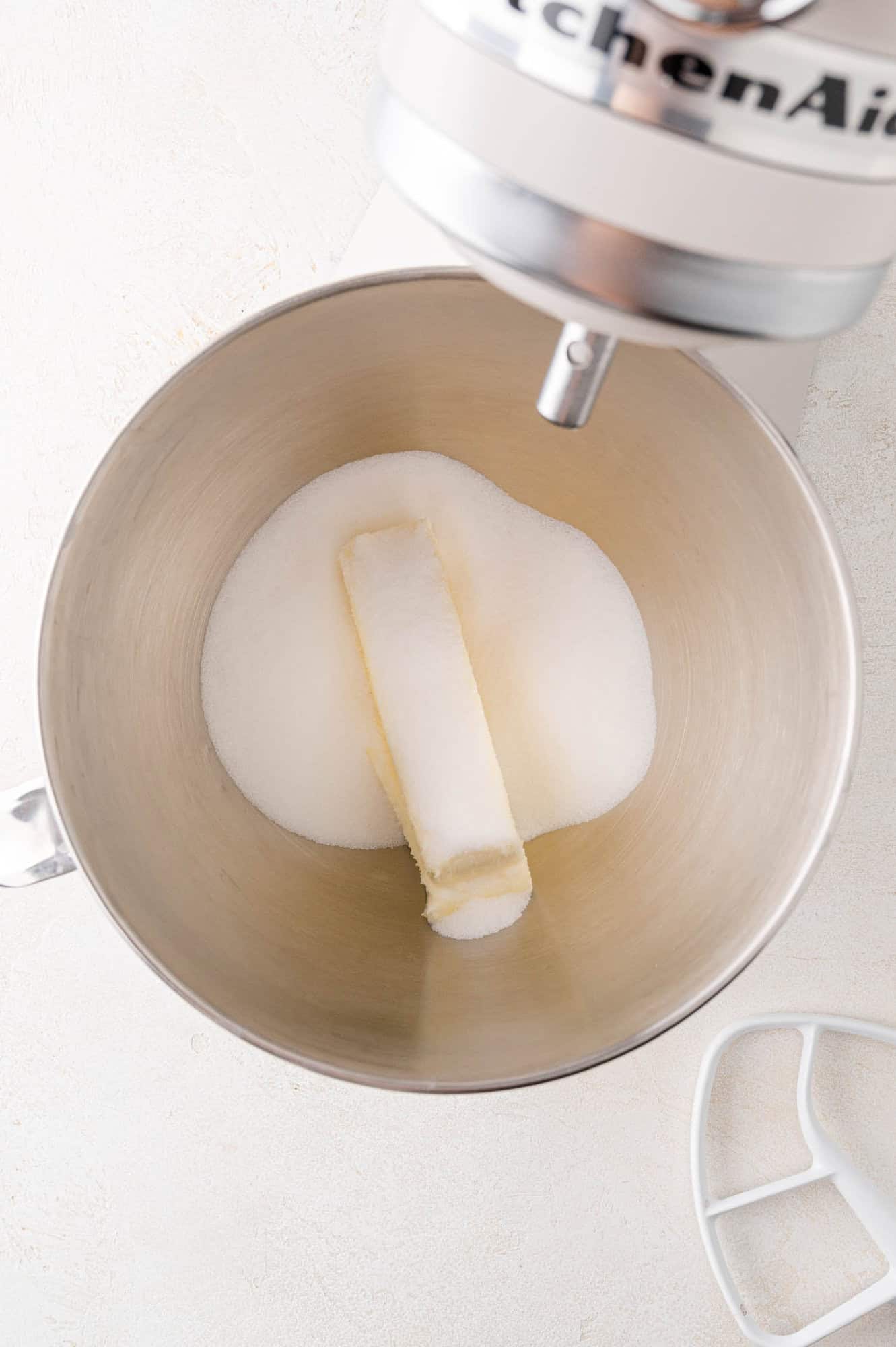 Bowl with a stick of butter and sugar in a stand mixer, viewed from above.