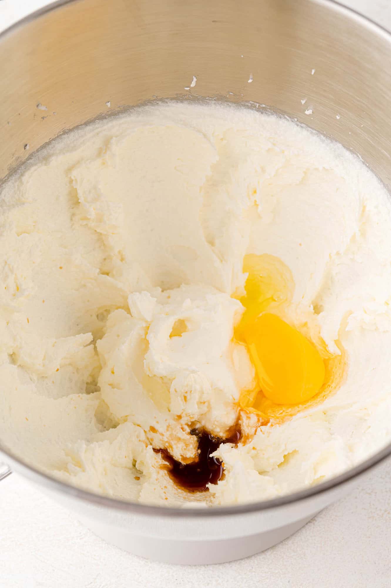 A mixing bowl contains whipped butter and sugar, an egg, and vanilla extract.
