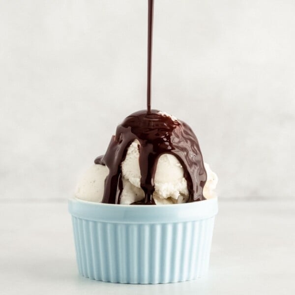 Vanilla ice cream in a blue cup with chocolate syrup being poured on top.