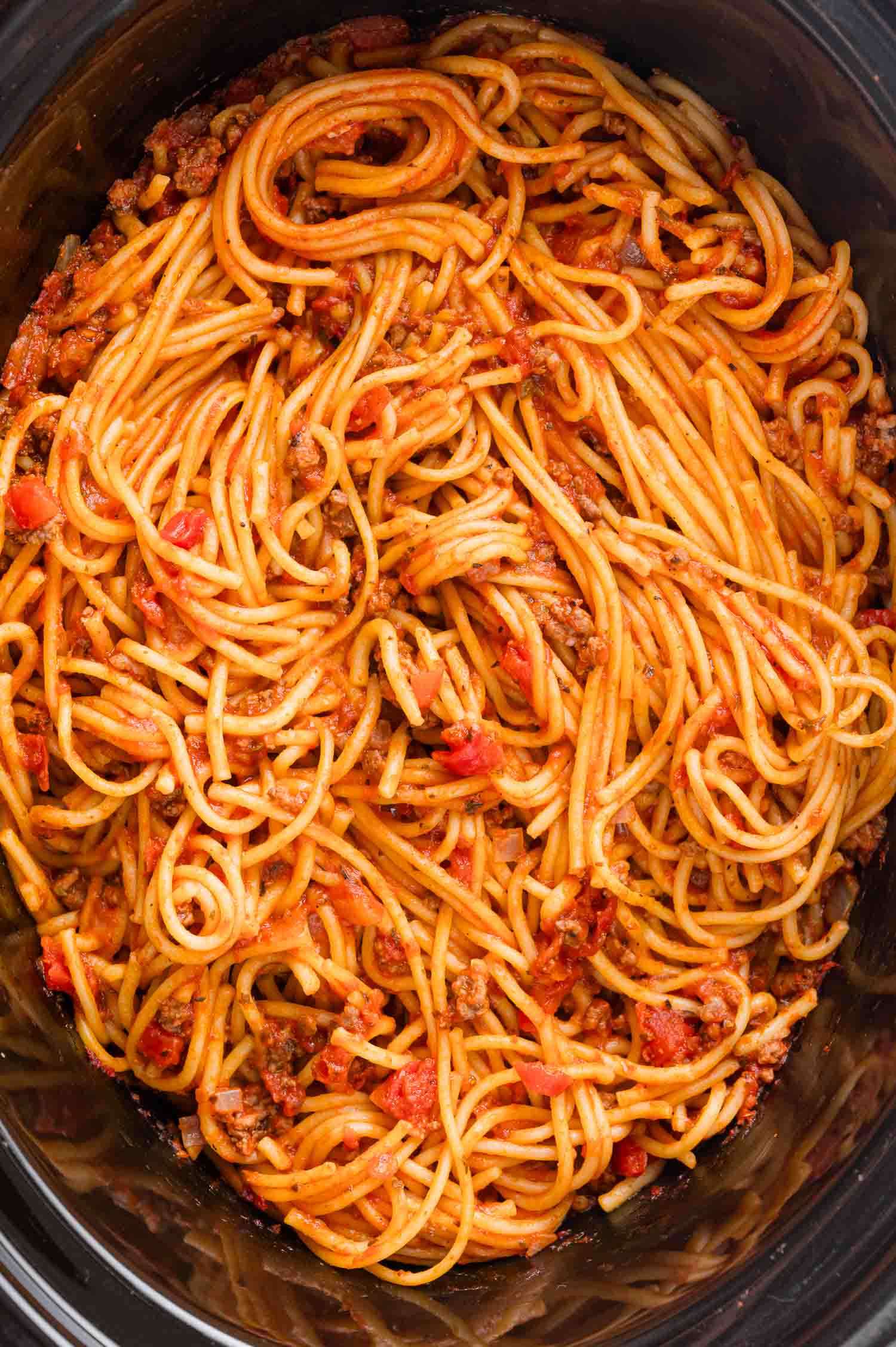 A close-up of spaghetti mixed with a tomato-based meat sauce in a large pot.