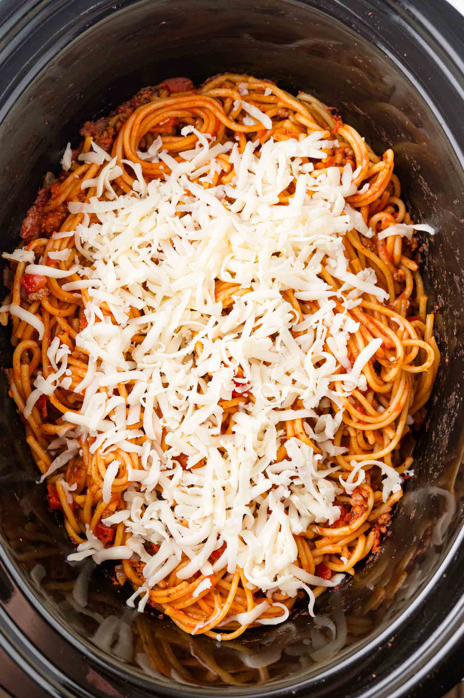 Spaghetti with meat sauce topped with shredded cheese in a slow cooker.