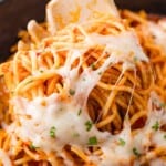 Close-up of spaghetti with melted cheese and herbs, twirled around a fork.