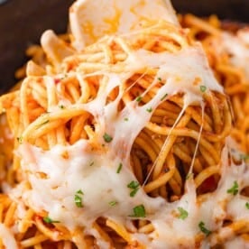 Close-up of spaghetti with melted cheese and herbs, twirled around a fork.