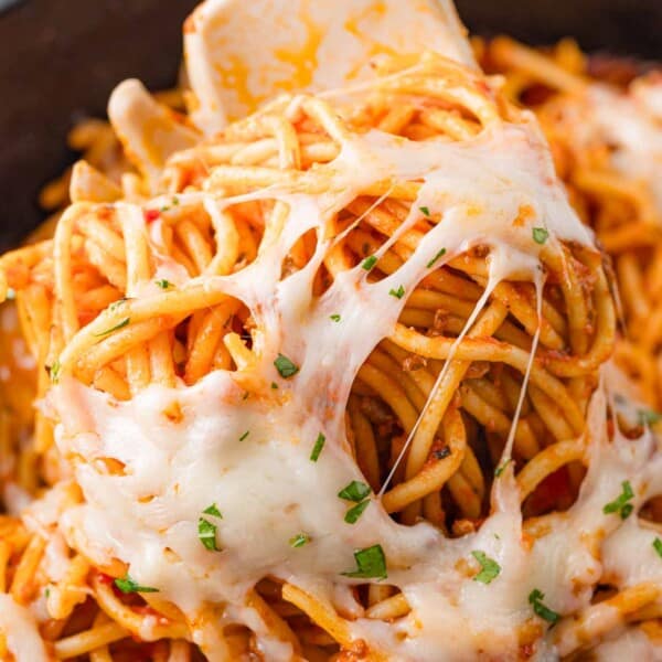 Close-up of spaghetti with melted cheese and herbs, twirled around a fork.