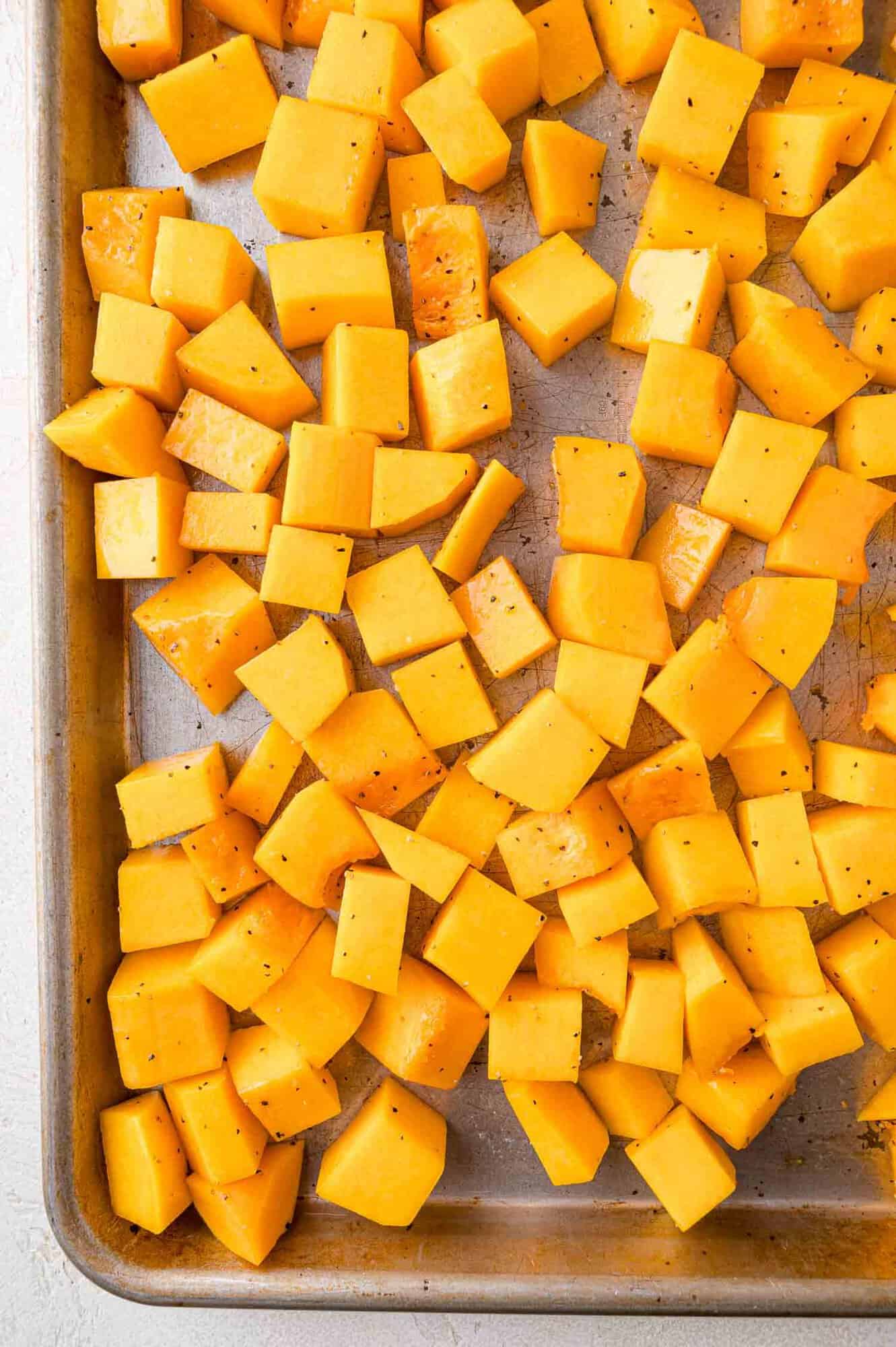 Cubed butternut squash seasoned with pepper on a baking sheet.