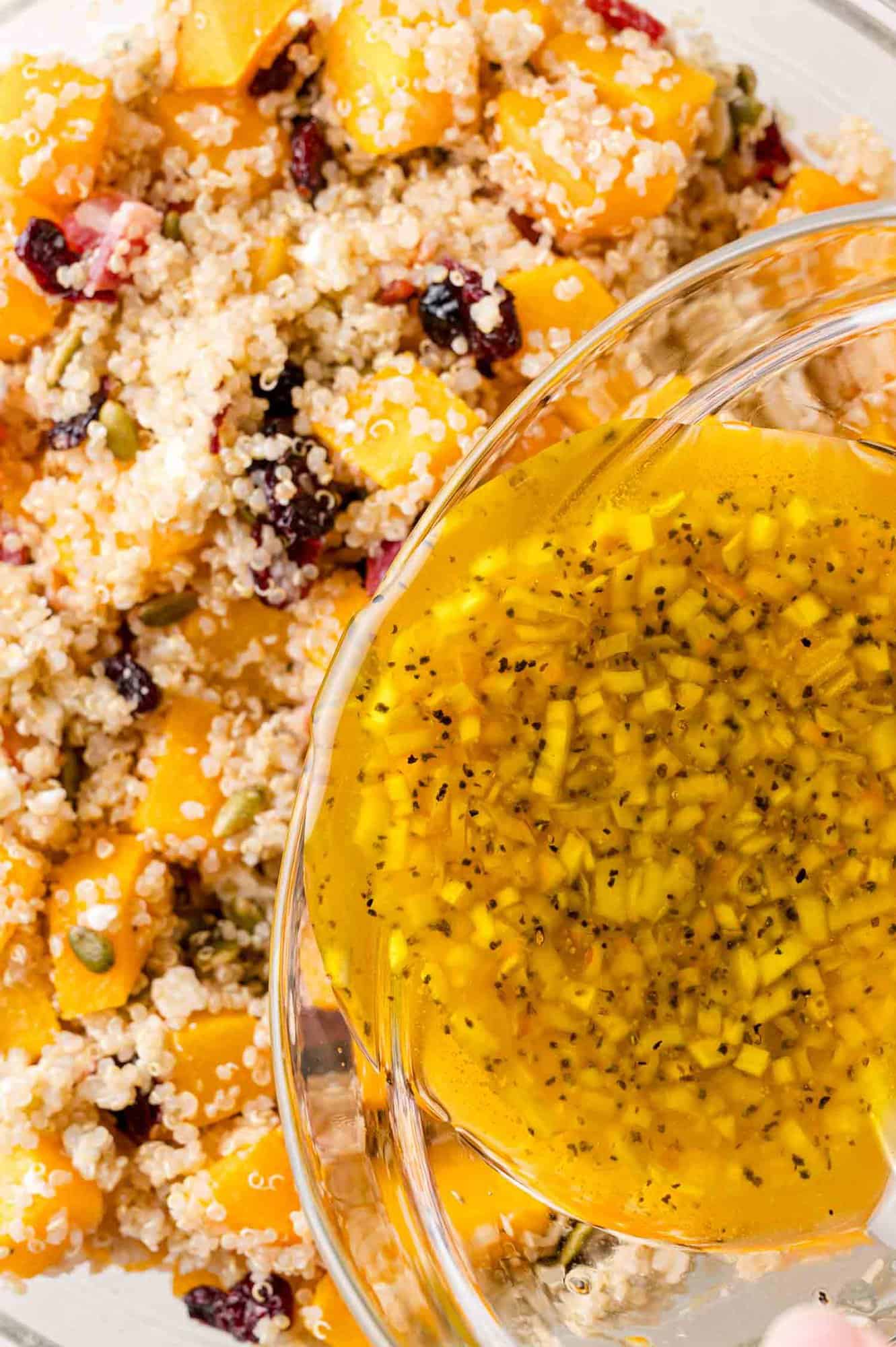 Close-up of a bowl of quinoa salad with squash and cranberries, dressing being poured on.