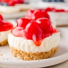 A no-bake cheesecake with a graham cracker crust, topped with red cherry topping, on a plate.