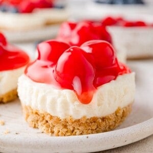 A no-bake cheesecake with a graham cracker crust, topped with red cherry topping, on a plate.