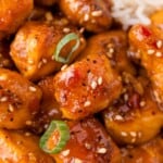 Close-up of glazed chicken pieces garnished with sesame seeds and sliced green onions.