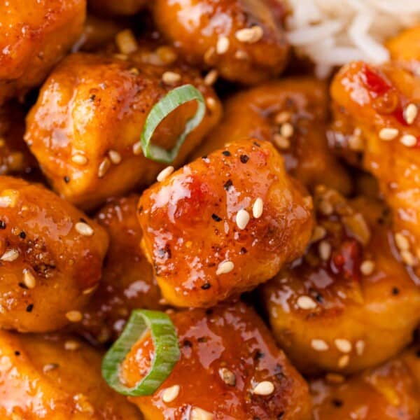 Close-up of glazed chicken pieces garnished with sesame seeds and sliced green onions.