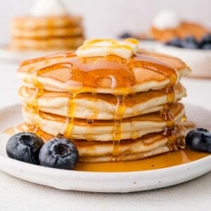 A stack of pancakes topped with butter and syrup on a plate, with blueberries beside them.