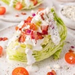 A wedge salad topped with blue cheese dressing, bacon bits, cherry tomatoes, and chopped red onions on a speckled plate.