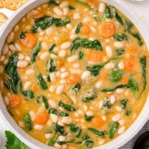 A pot of white bean soup, spinach, carrots, and a creamy broth.