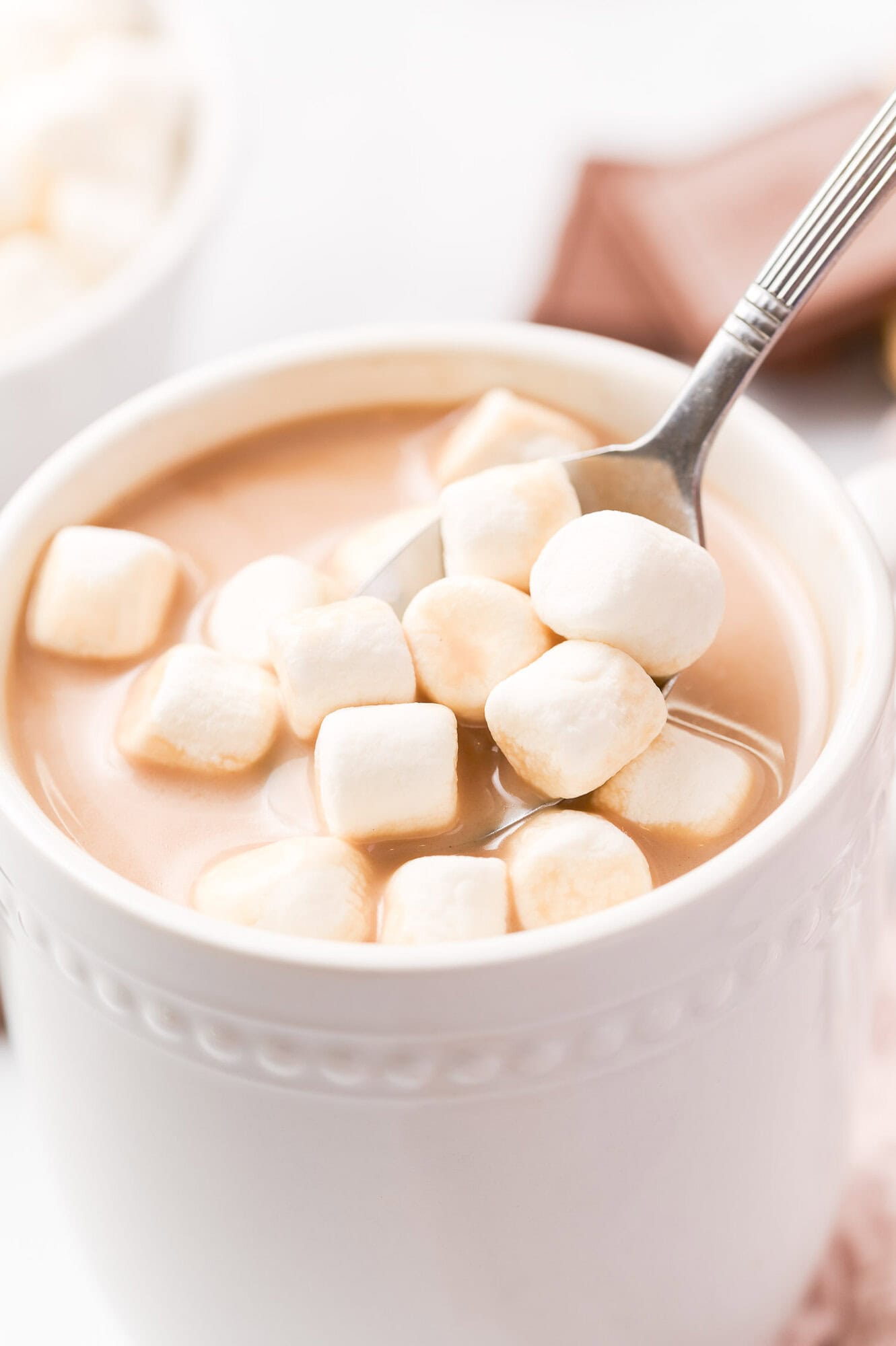 A mug of hot chocolate topped with mini marshmallows and a spoon.
