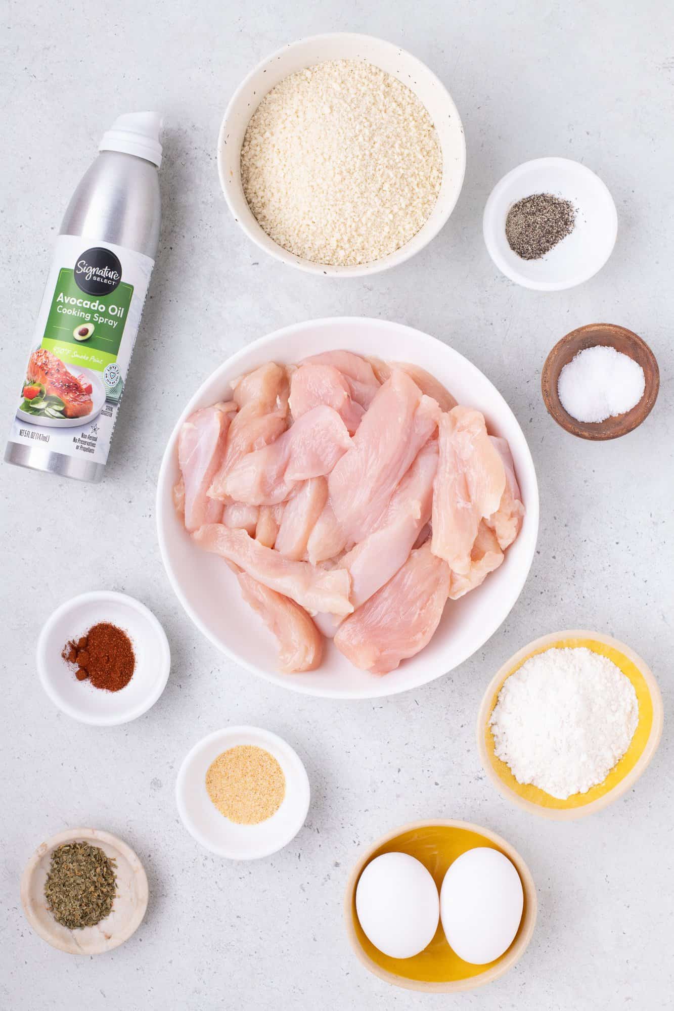 Ingredients for chicken tenders: raw chicken strips, avocado oil spray, breadcrumbs, eggs, flour, spices.
