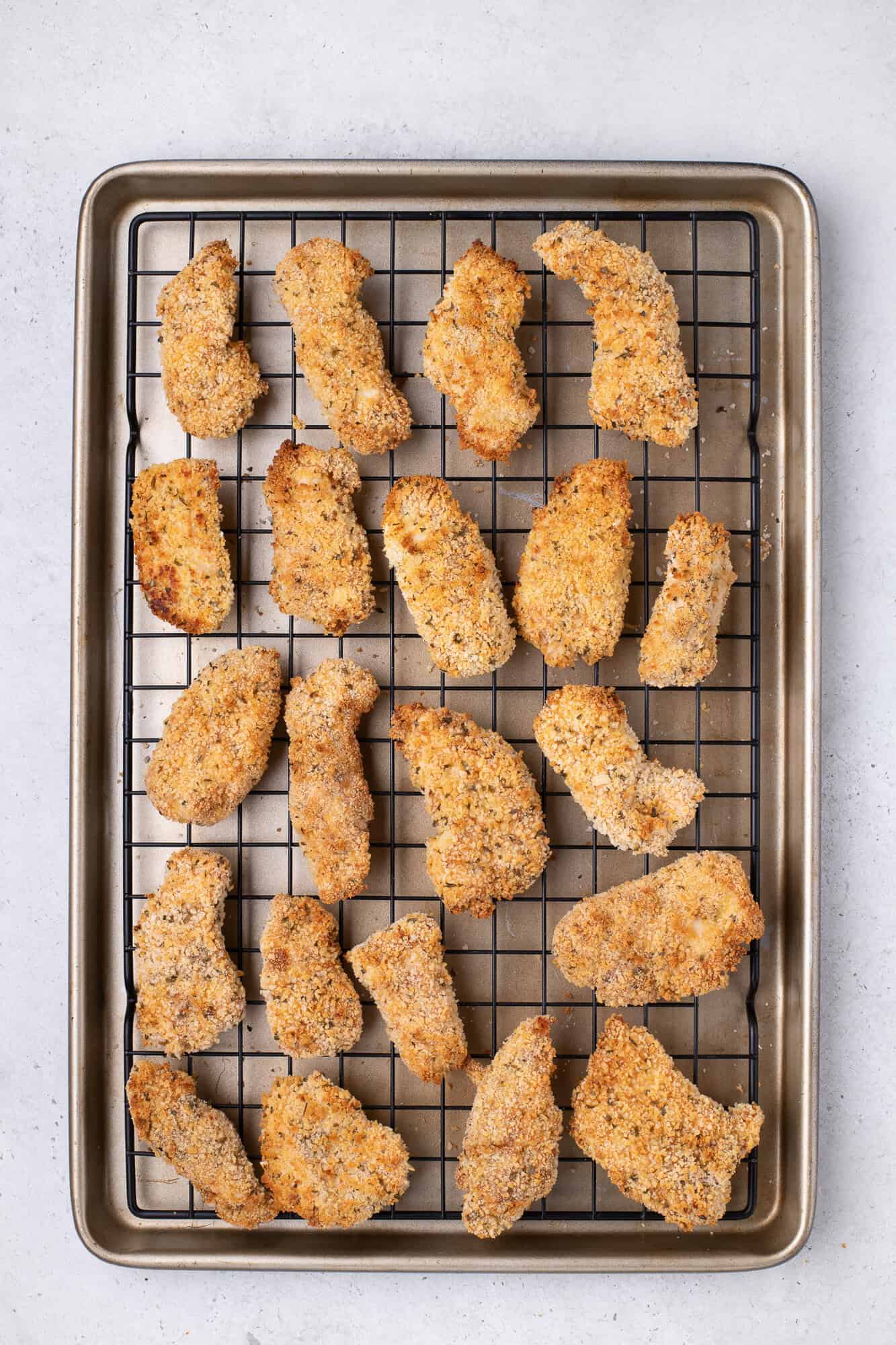 Baked breaded chicken pieces on a wire rack over a baking tray, set against a light background.
