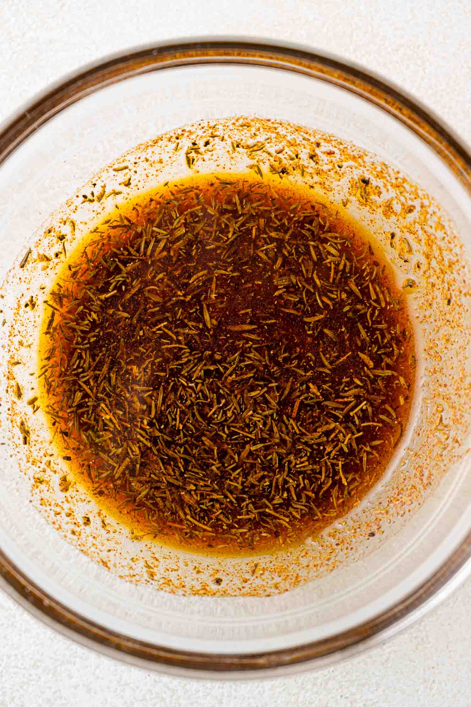 A glass bowl containing a brown liquid mixture with herbs and spices.