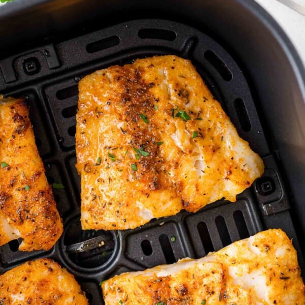 Close-up of seasoned fish fillets in an air fryer basket, with a golden-brown, crispy texture.