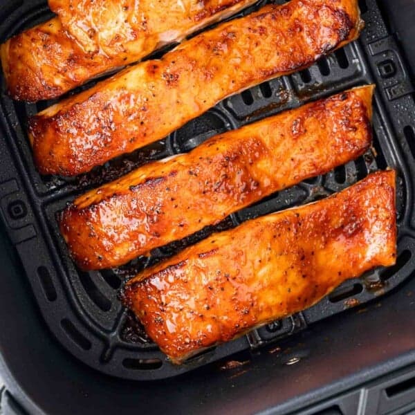 Four glazed salmon fillets in an air fryer basket, cooked to a golden brown.