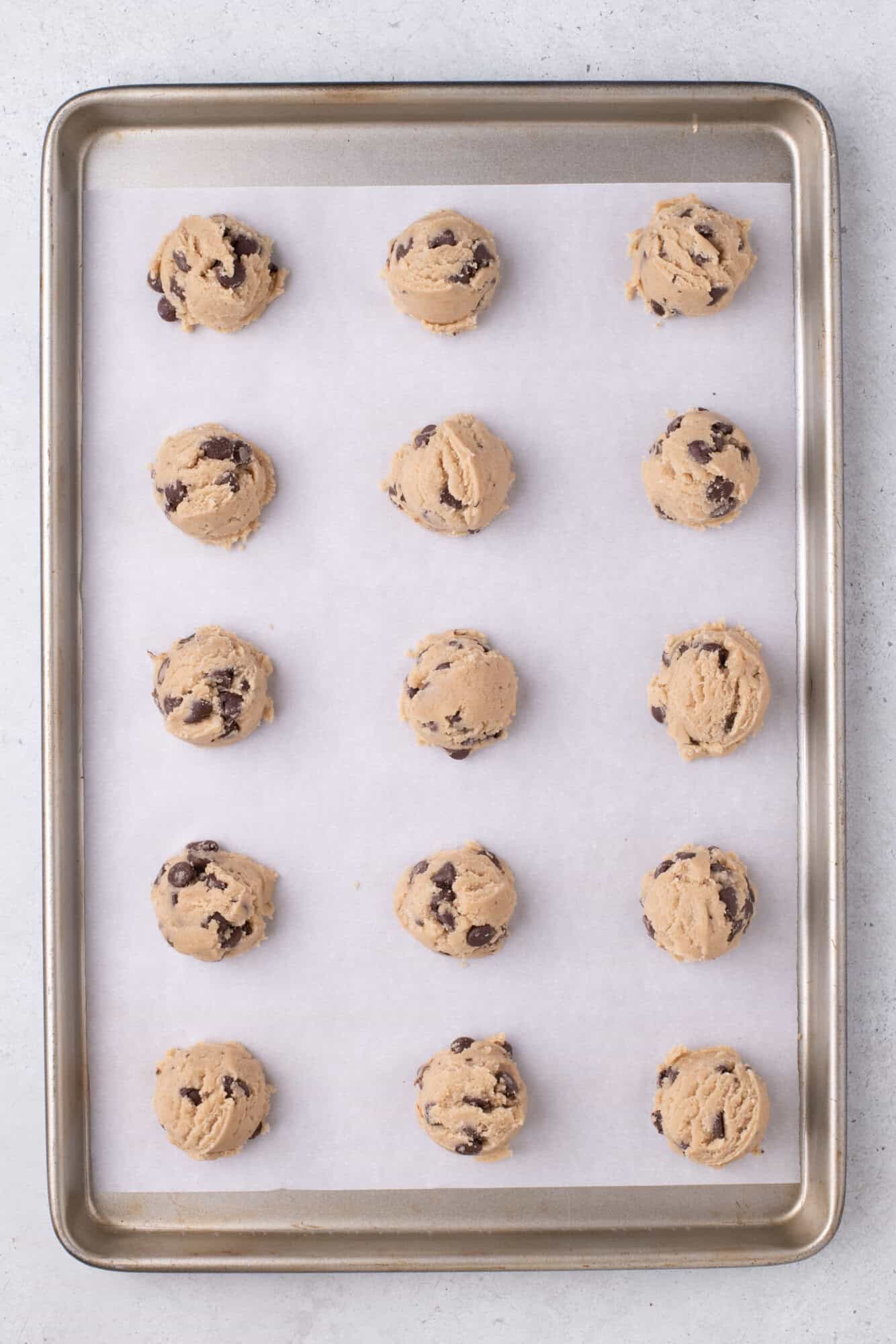 Cookies with chocolate chips are evenly spaced on a parchment-lined baking sheet, ready to be baked.