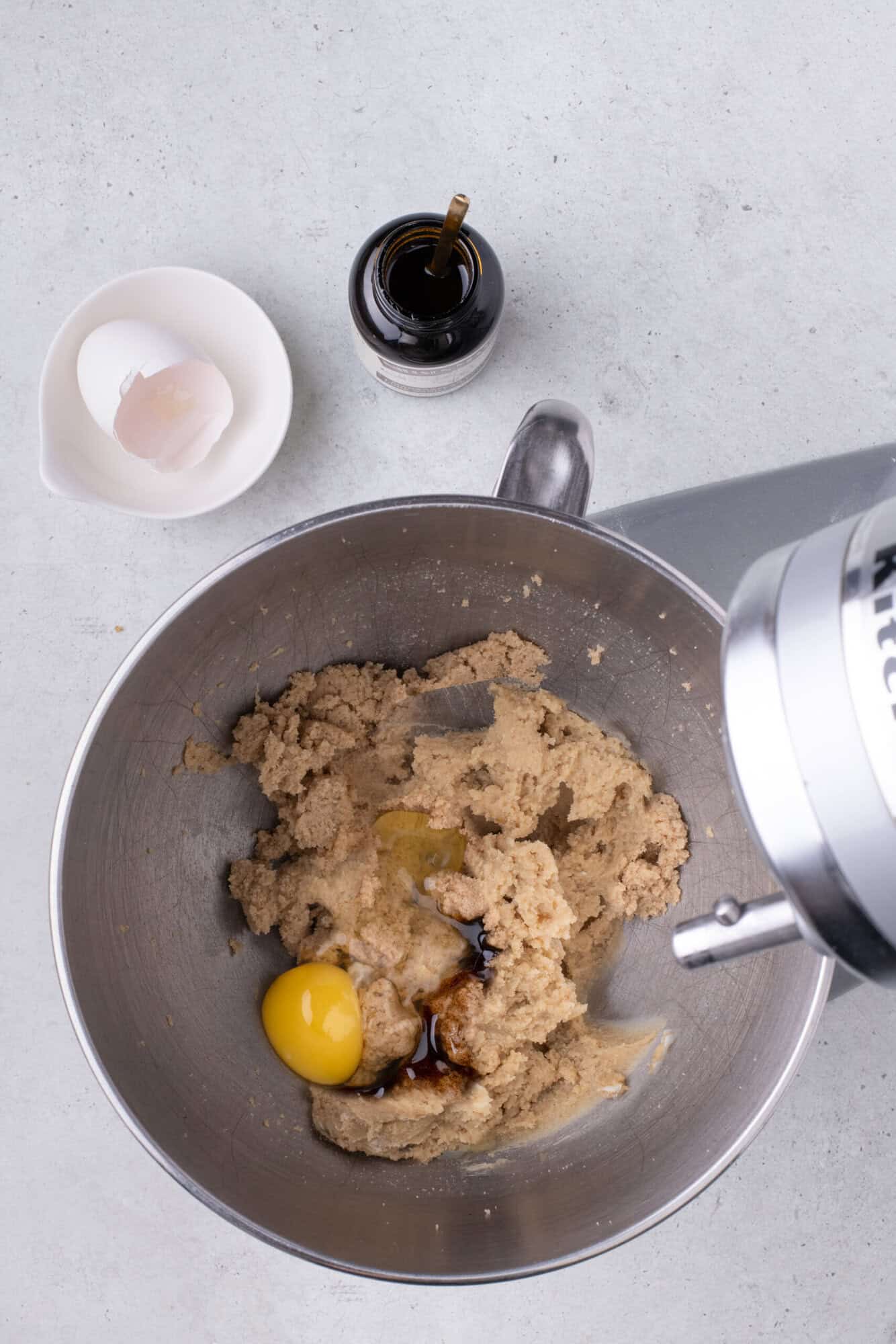 Mixing bowl with cookie dough, an egg, and vanilla extract. An empty eggshell is beside the bowl.