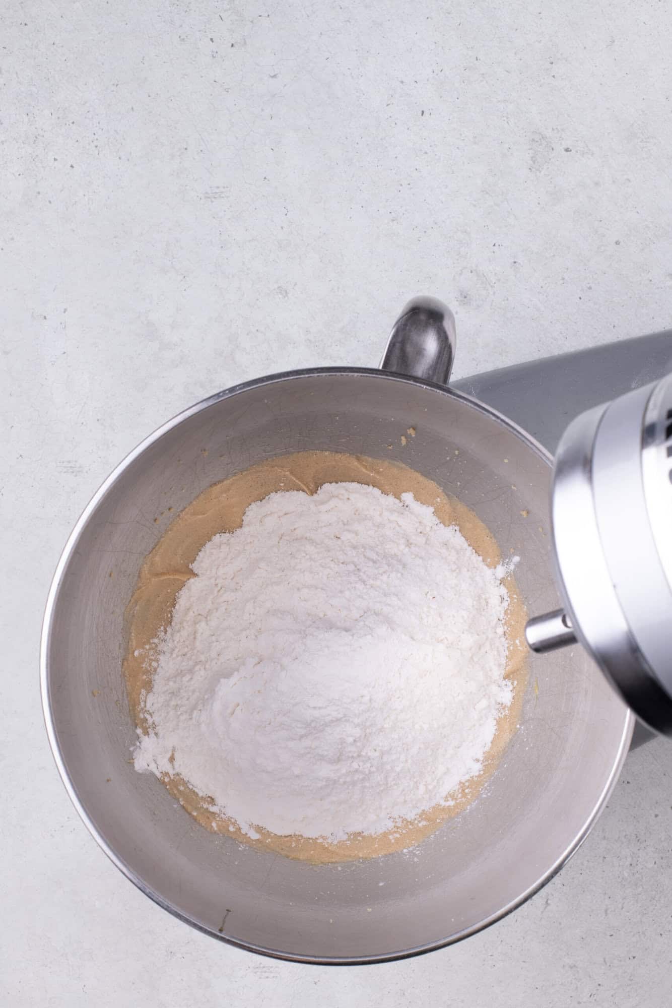 A mixing bowl with flour and batter inside, placed on a countertop, attached to a stand mixer.