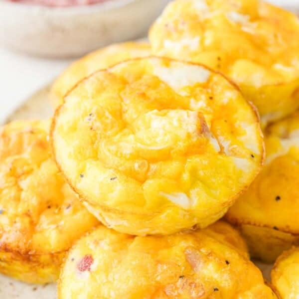 Close-up of a stack of baked egg muffins with a golden-brown top, featuring visible pieces of ham and cheese.