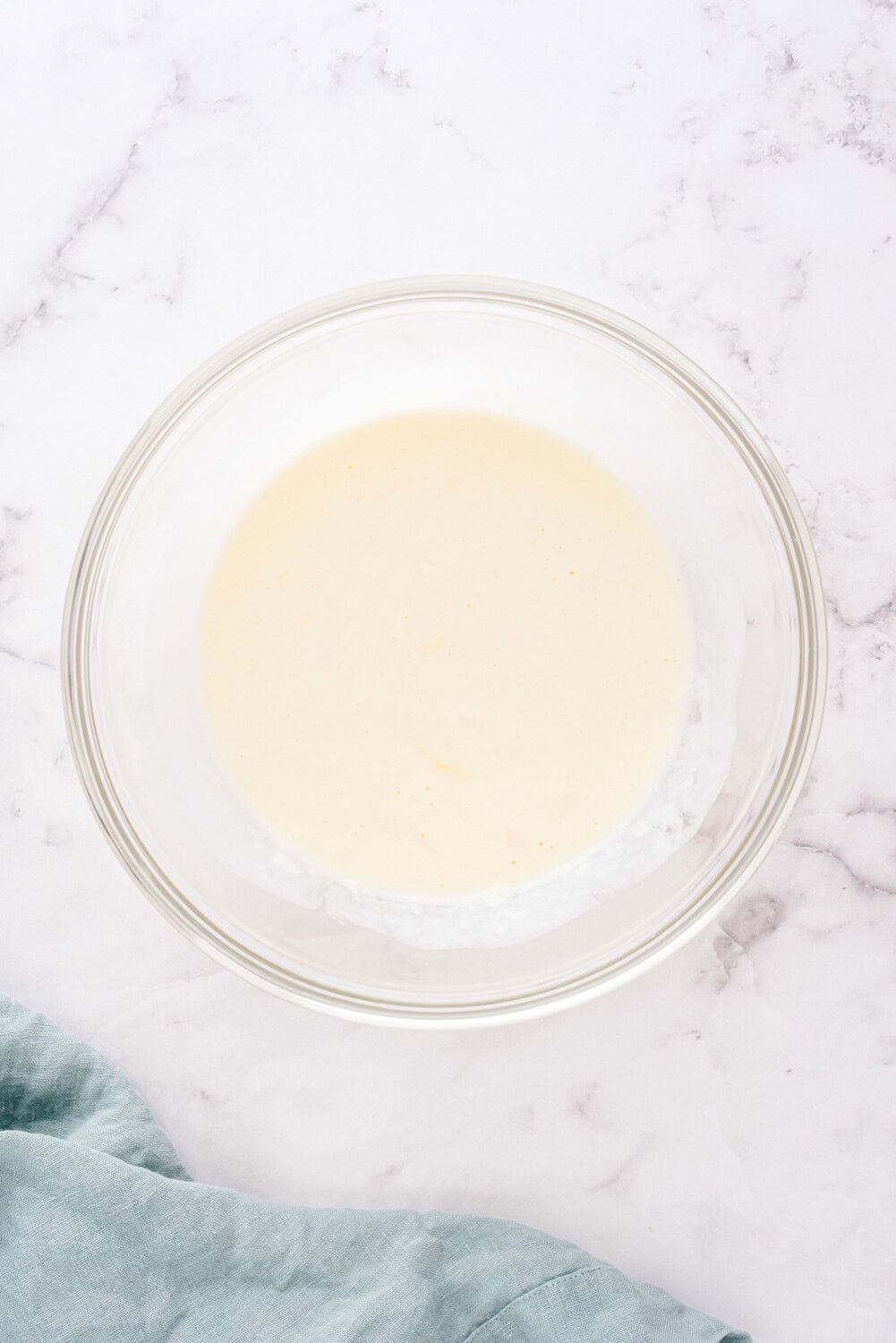 A glass bowl filled with light-colored liquid on a marble surface, partially covered by a green cloth at the bottom left.