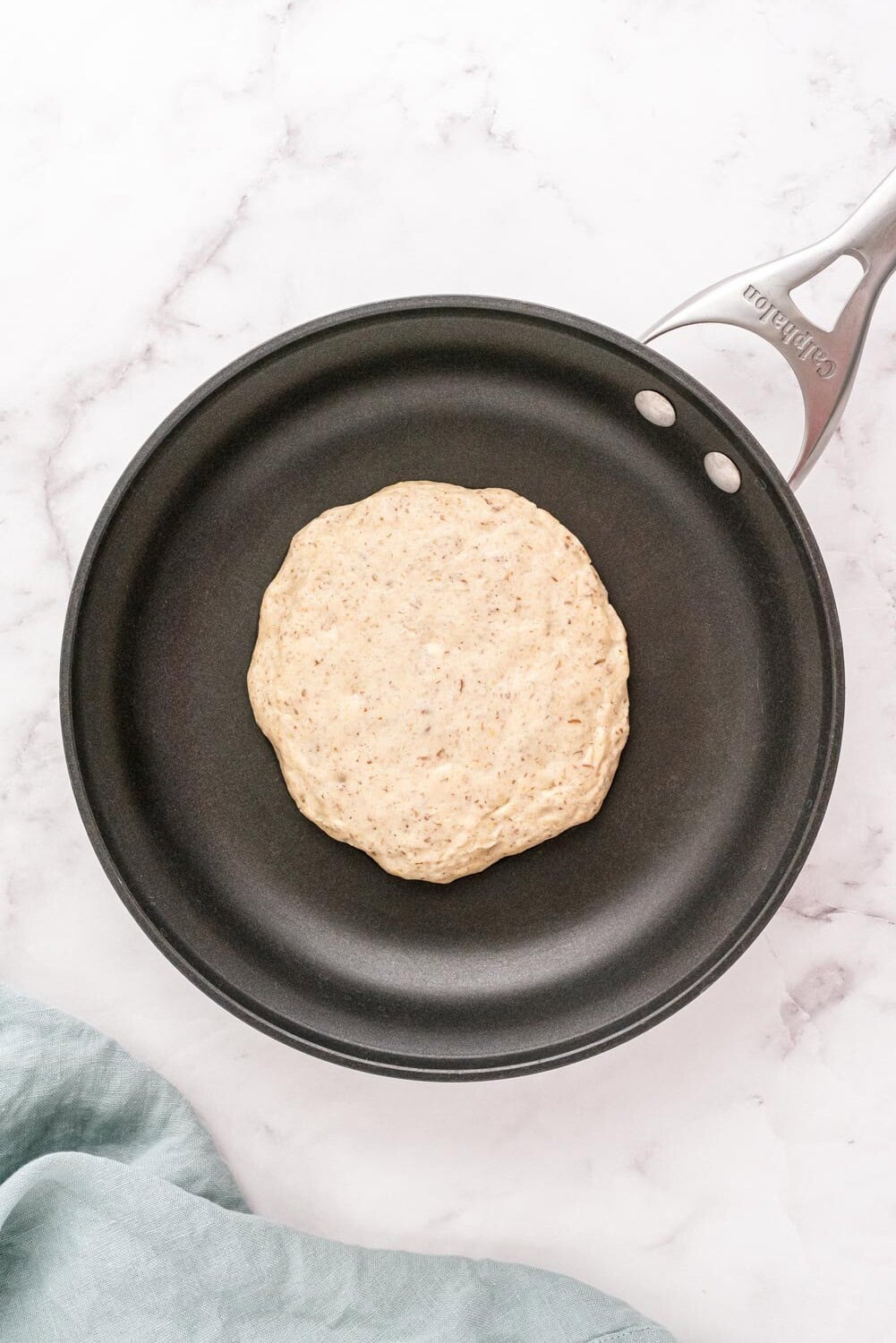 A pancake batter cooking in a black frying pan on a marble countertop.