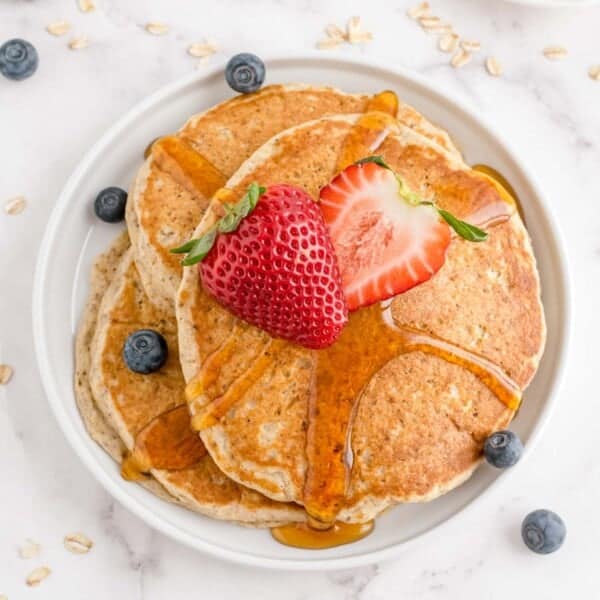 A plate of pancakes topped with sliced strawberries and blueberries, drizzled with syrup.