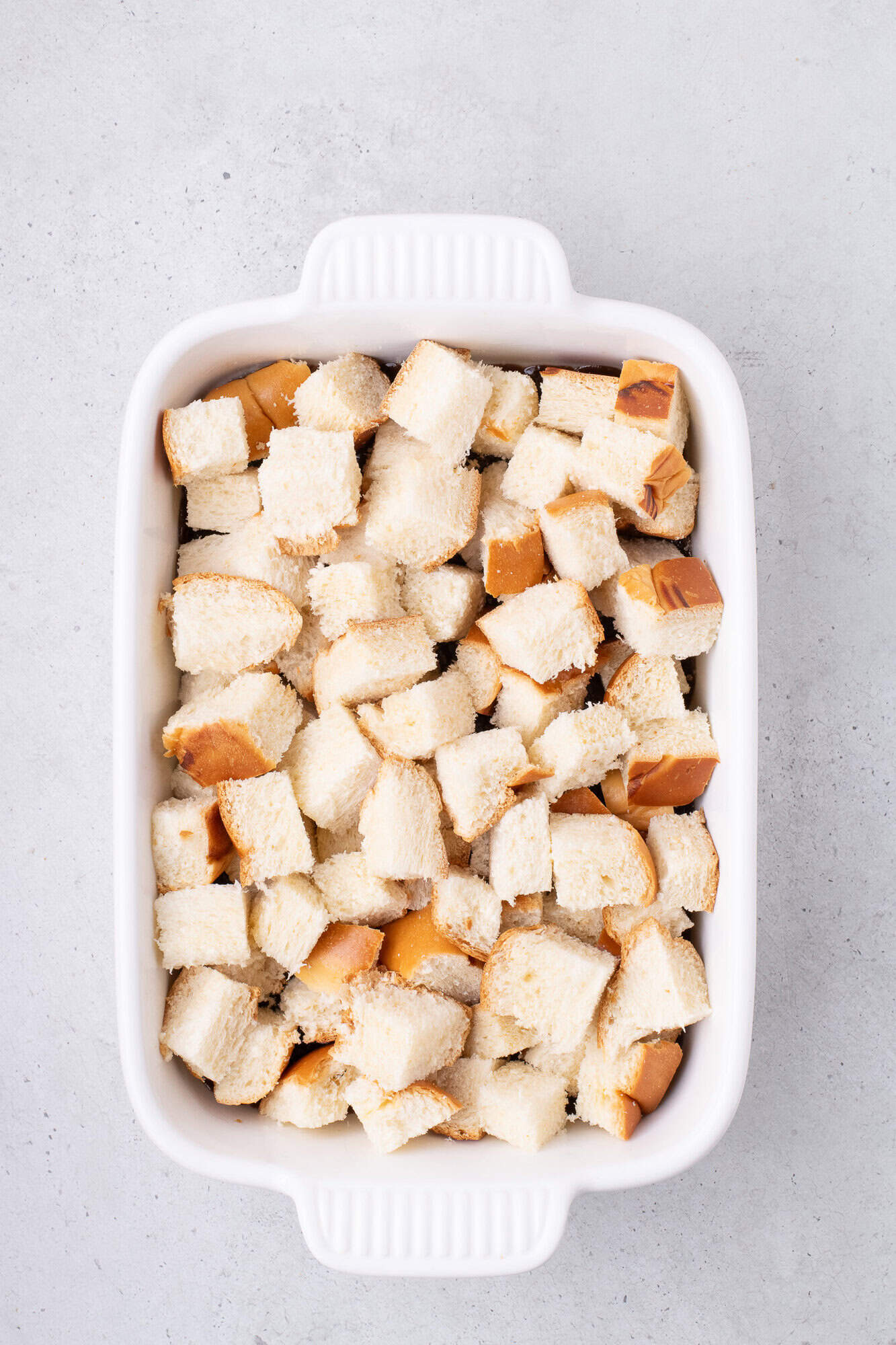 A white baking dish filled with evenly arranged bread cubes.
