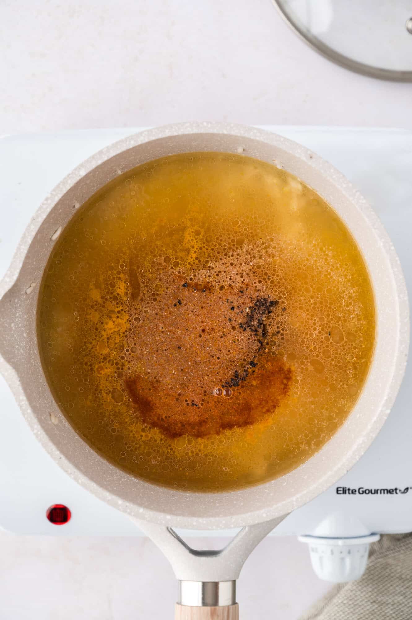 Pot of boiling broth on a stovetop with bubbling spices and herbs visible on the surface.