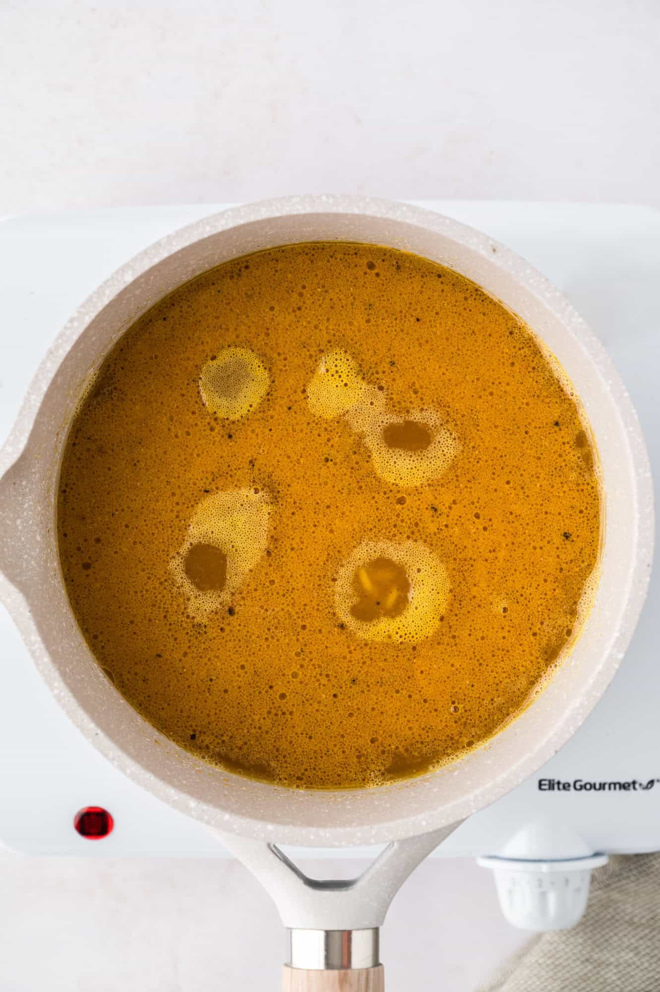 A saucepan with simmering broth sits on a white stovetop.