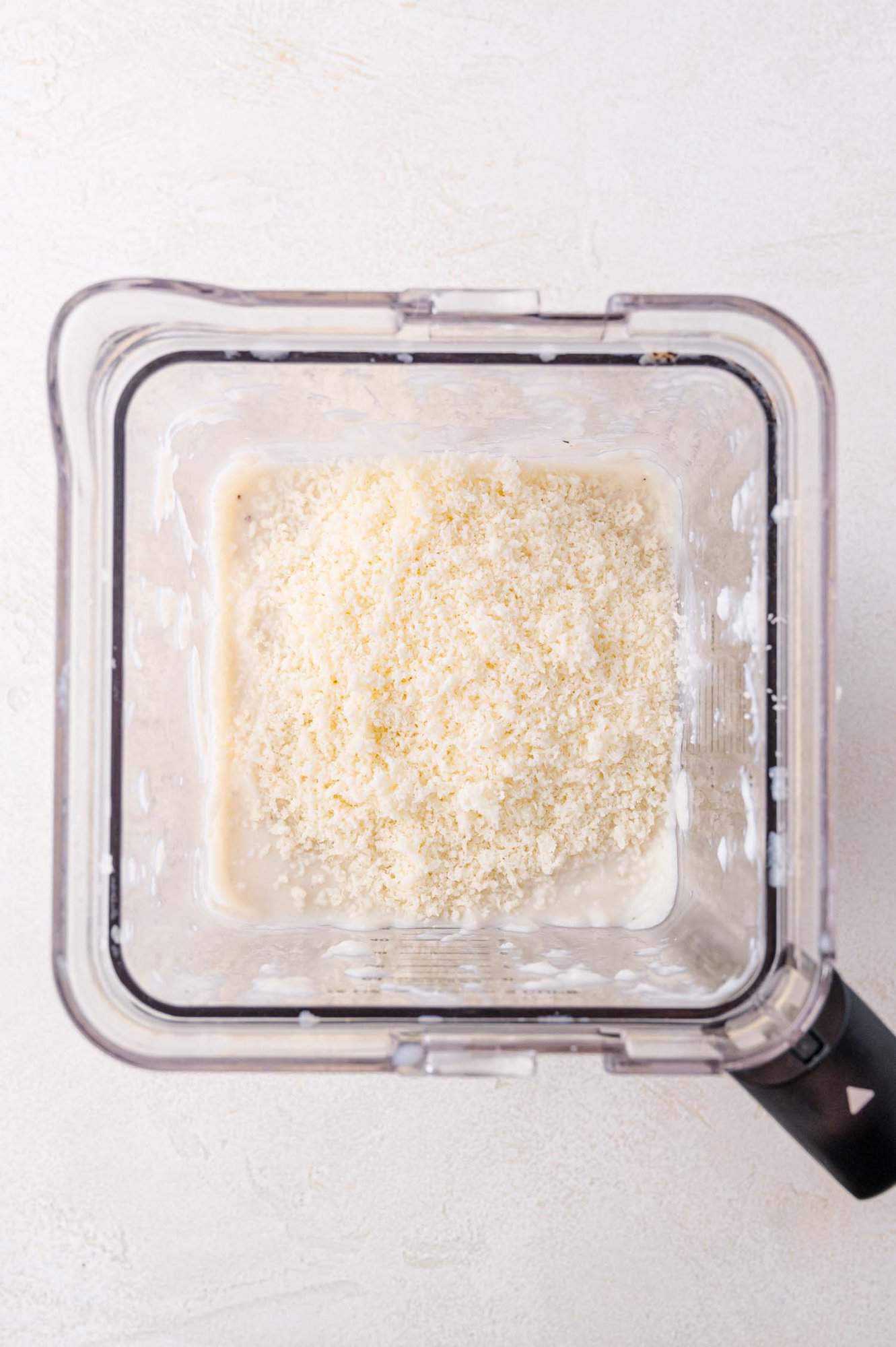 A blender filled with a creamy mixture and finely grated cheese, viewed from above.