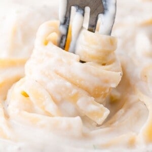 A fork twirls creamy fettuccine noodles in a white sauce.