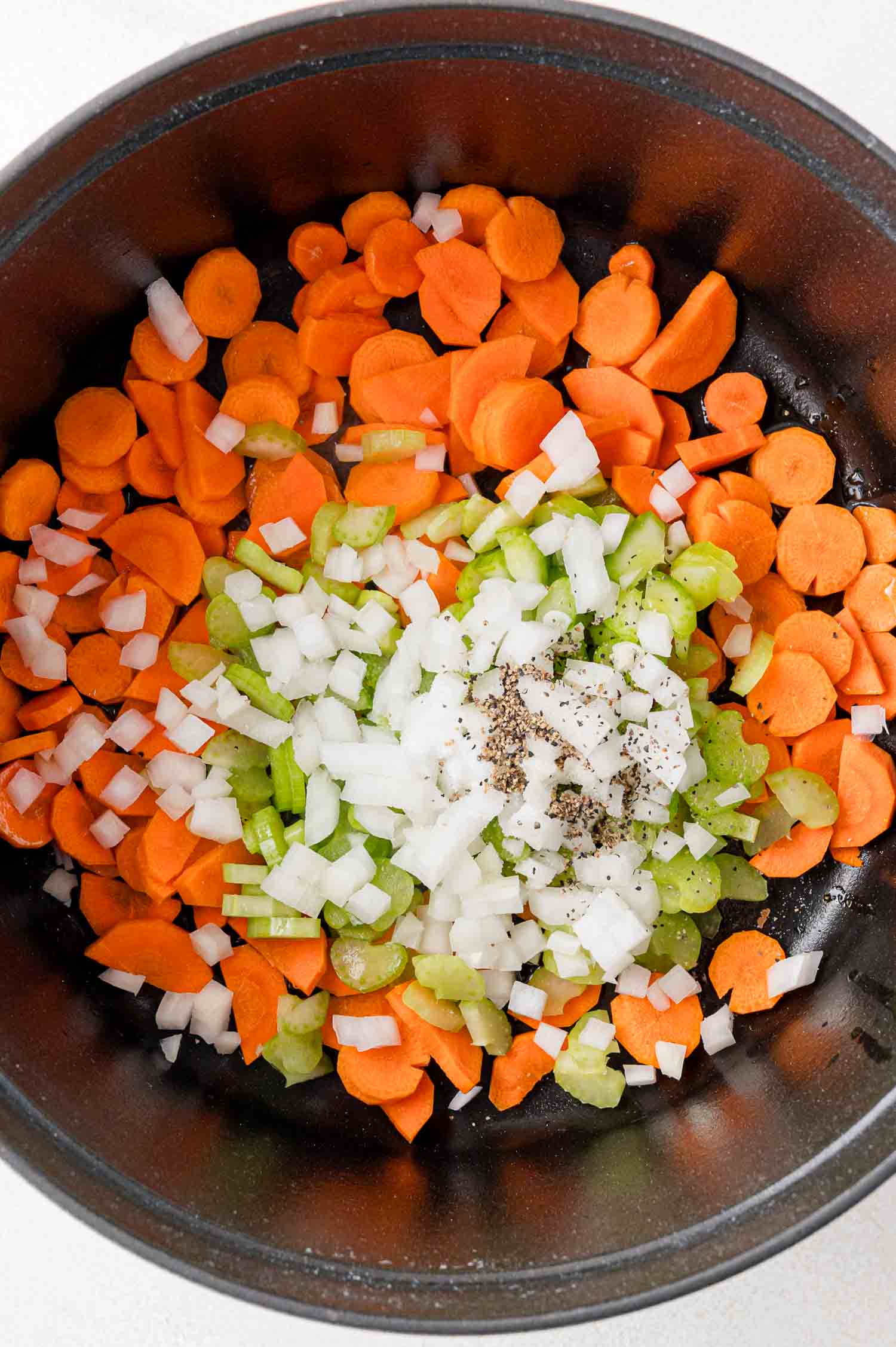 Chopped carrots, celery, and onions with pepper in a pot.