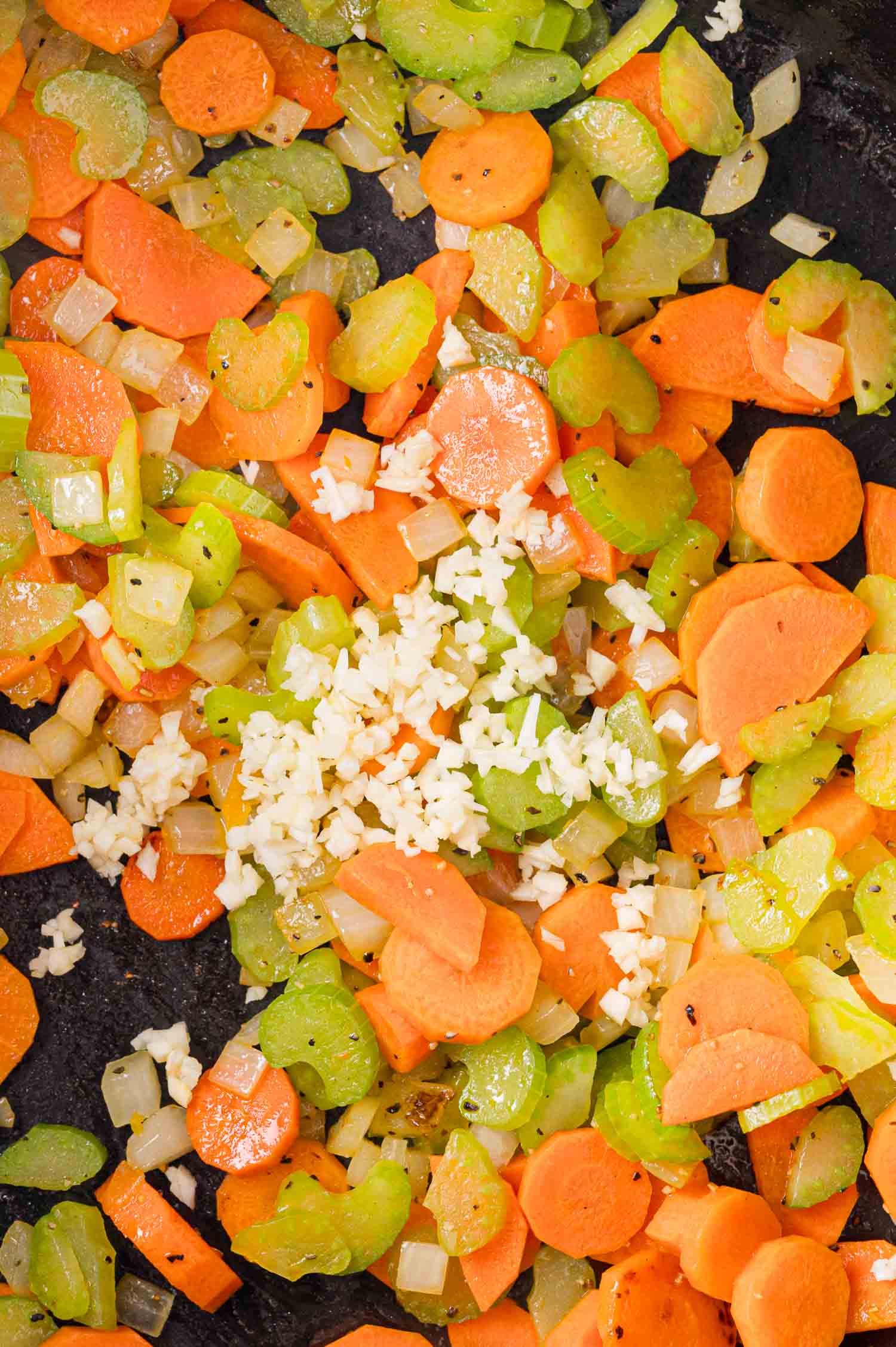 Chopped carrots, celery, onions, and minced garlic sautéed in a pan.